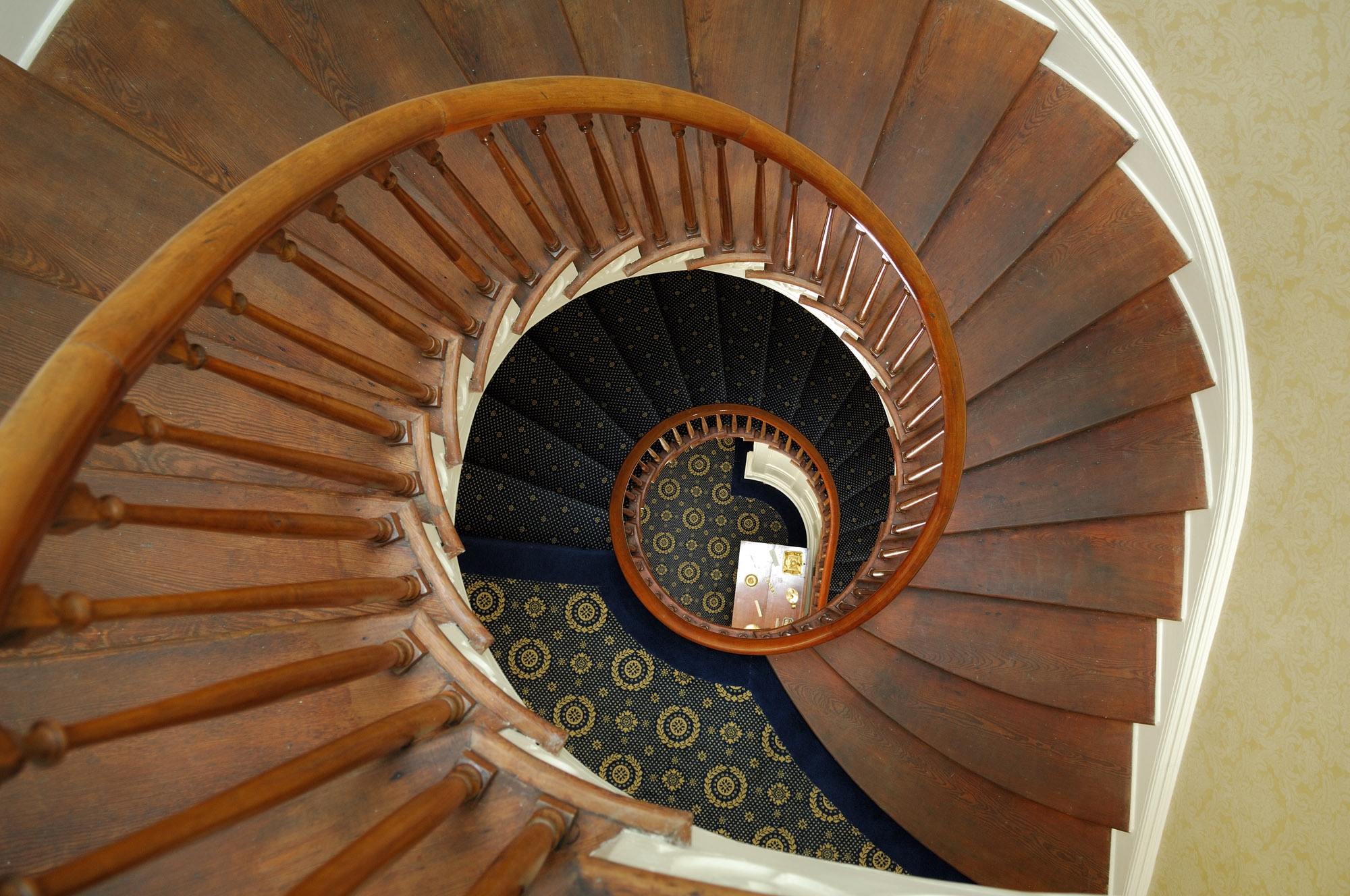 A cantilevered spiral staircase curving upward through three floors toward a glass cupola